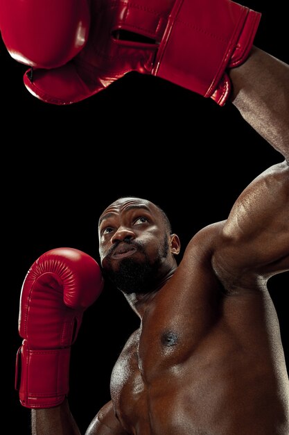 Mãos de boxeador sobre fundo preto. Conceito de força, ataque e movimento. Ajuste o modelo afro-americano em movimento. Atleta afro-musculoso em uniforme esporte. Homem desportivo durante o boxe