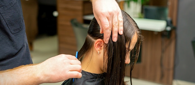 Mãos de cabeleireira penteando o cabelo de uma jovem repartidas em secções na barbearia