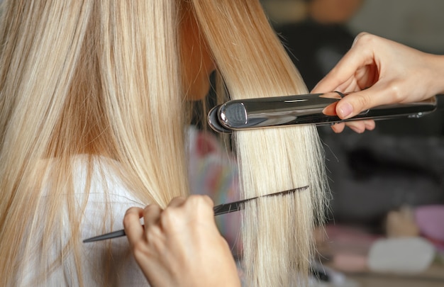 Mãos de cabeleireiro alisa o cabelo com modelador