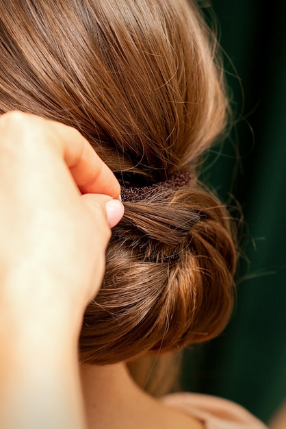 Mãos de cabeleireiro fazendo penteado de torção francesa de uma jovem morena irreconhecível em um salão de beleza, vista traseira, close-up.