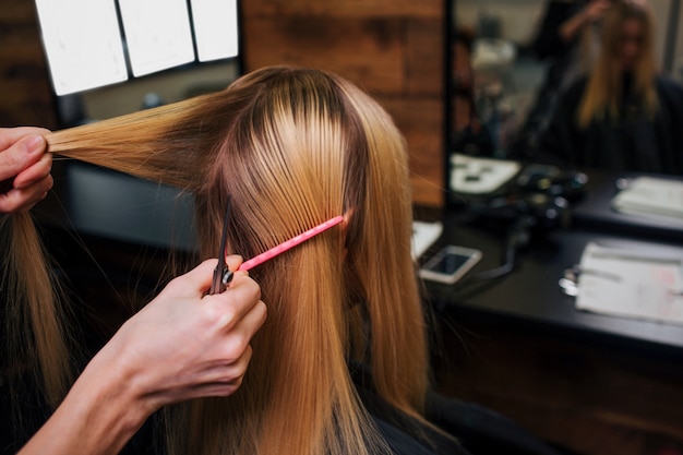 Mãos de cabeleireiro segurando uma mecha de cabelo loiro enquanto penteava antes do corte de cabelo