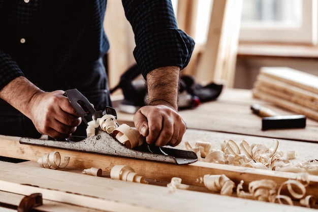 Mãos de carpinteiro aplainando uma prancha de madeira com uma plaina manual