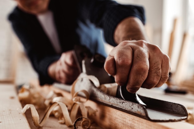 Foto mãos de carpinteiro aplainando uma prancha de madeira com uma plaina manual