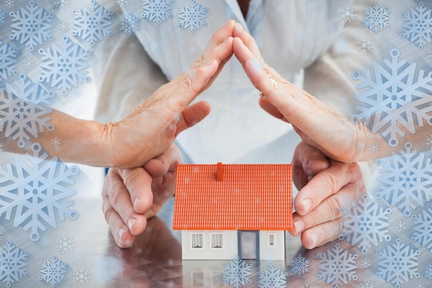 Mãos de casais com casa modelo contra quadro de floco de neve