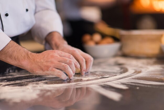 mãos de chef preparando massa para pizza polvilhada com mesa de farinha closeup