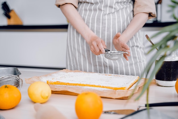 Mãos de chefs com peneira pequena para assar Baker decorando e polvilhando bolo de laranja ou torta com açúcar em pó Fundo de cozinha produtos de padaria caseiros e artesanais