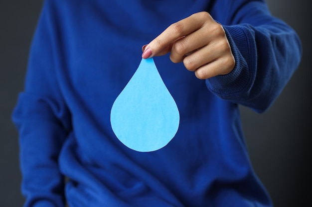 Mãos de close-up no suéter azul segurando a gota de água de papel. Dia Mundial da Água, economize a água.