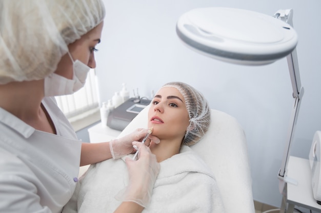 Foto mãos de cosmetologista fazendo injeção no rosto, lábios