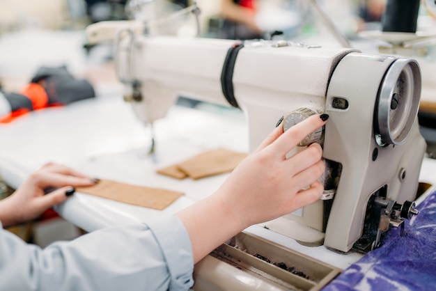 Mãos de costureira feminina costura tecidos em uma máquina de costura. alfaiataria ou corte e costura em fábrica de roupas, bordado, costureira em oficina