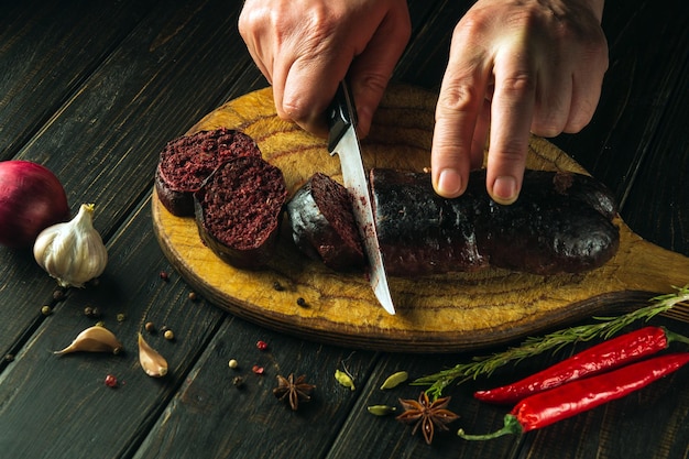 Foto mãos de cozinheiro em close-up com uma faca cortando salsicha de sangue em uma tábua de corte da cozinha cozinhando um prato nacional com especiarias em casa na cozinha