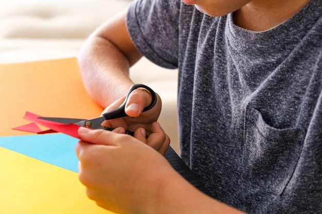 Mãos de criança, corte de papel colorido com uma tesoura na mesa