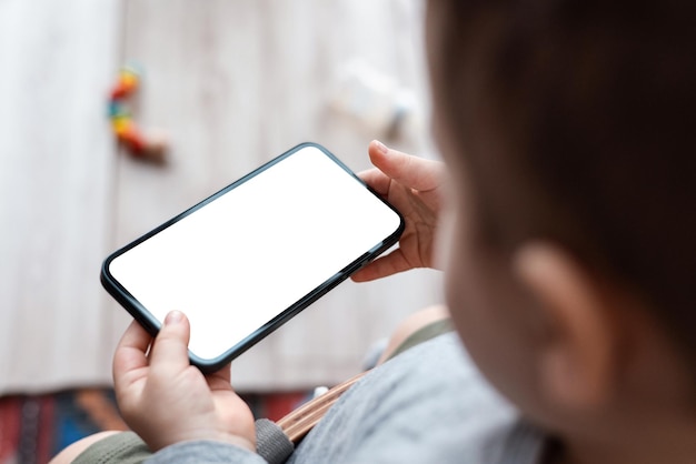 Mãos de criança de meninos segurando o telefone no fundo de casa as mãos da criança seguram smartphone preto e assist...