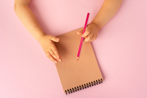 Mãos de criança escrevendo em um caderno aberto, vista superior