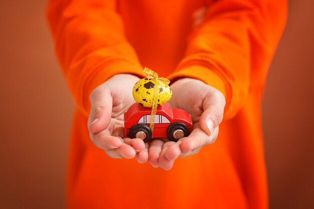 Mãos de criança segurando um ovo de Páscoa no carro em fundo laranja. Conceito de feliz Páscoa.