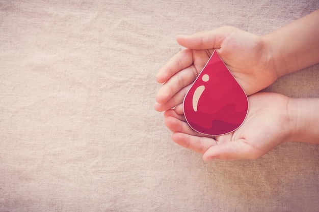 Mãos de criança segurando uma gota de sangue