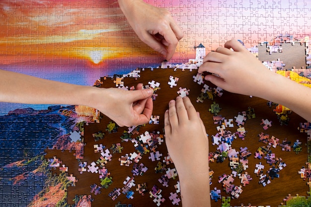 Foto mãos de crianças e adultos empilham quebra-cabeças de cores na mesa de madeira