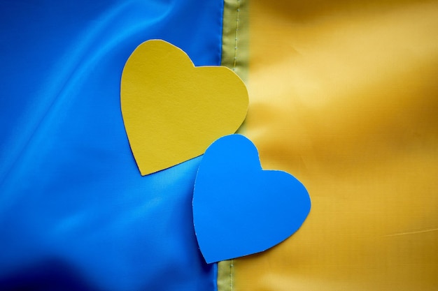 Mãos de crianças segurando corações de papel amarelo-azul no fundo da bandeira ucraniana