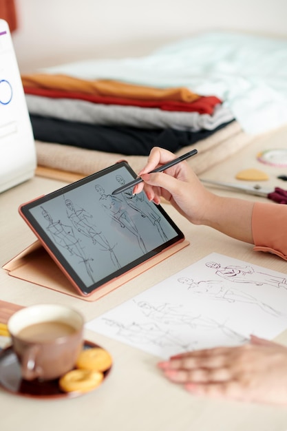 Mãos de designer de moda ou alfaiate desenhando esboços no computador tablet para mostrar sua ideia ao cliente