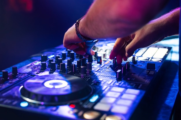 Mãos de dj misturam música em uma mesa de mixagem em uma boate