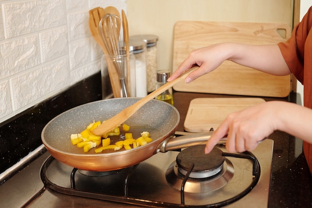 Mãos de dona de casa fritando legumes na frigideira enquanto cozinha um prato delicioso para o jantar