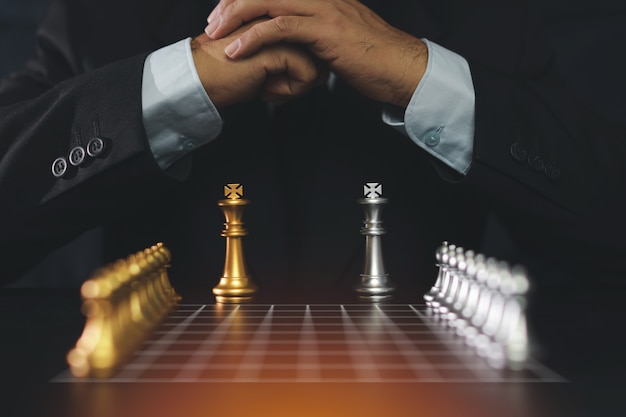 Mãos de empresário na suíte preta, sentado e segurando as mãos, planejando a estratégia com xadrez na mesa vintage. Conceito de objetivo de decisão e conquista.