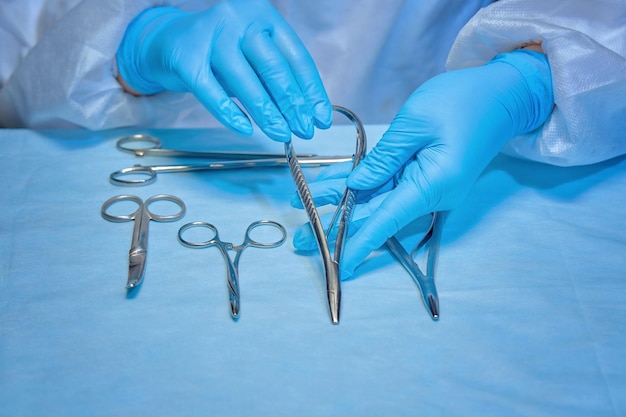 Mãos de enfermeira de uniforme e luvas com um instrumento para cirurgia ou curativo na mesa