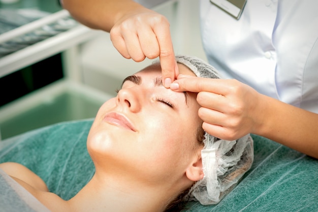 Mãos de esteticista fazem massagem na sobrancelha de uma mulher enquanto uma massagem facial no centro de clínica de cosmetologia