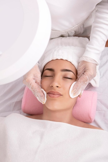 Mãos de esteticista realizando limpeza facial aplicando tônico com almofadas de algodão conceito de cuidados com a pele