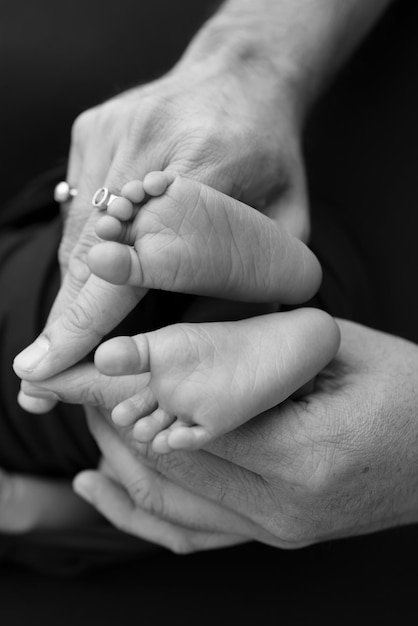 Mãos de forma bonita de sombra preto e branco da mãe seguram pés minúsculos de bebê recém-nascido em fundo preto com cuidado amoroso segurança familiar e proteção criança com conceito de nascimento prematuro ou cuidado de UTIN