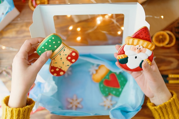 Mãos de garotas com suéter tricotado segurando pão de mel de Natal com biscoitos de confeiteiro em forma de meia e ...