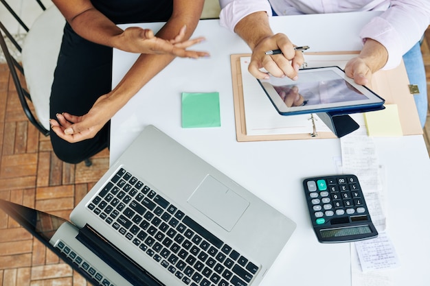 Mãos de gerentes financeiros discutindo relatórios e diagramas no computador tablet na reunião, vista de cima