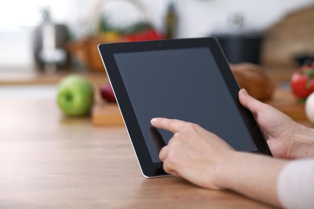 Mãos de Haman usando o touch pad na cozinha. Closeup de mulher fazendo compras on-line por computador tablet e cartão de crédito. Conceito de cozinha e compras.