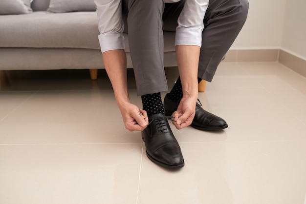 Mãos de homem amarrando o cadarço de seus sapatos novos. Conceito de pessoas, negócios, moda e calçados - close-up da perna do homem e mãos amarrando cadarços de sapato.