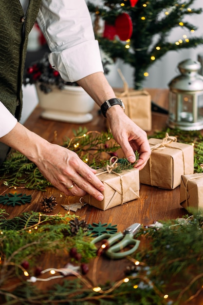 Mãos de homem amarrando uma caixa de presente de artesanato de Natal com um galho de abeto na mesa de madeira
