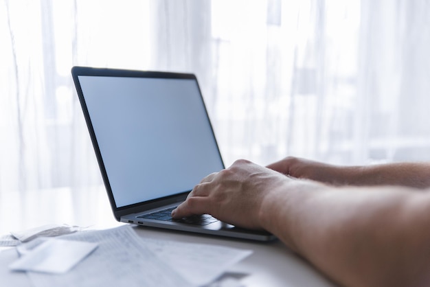 Mãos de homem digitando no laptop de teclado com laptop de tela branca parece macbook