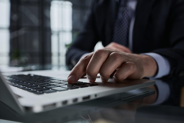 Mãos de homem digitando no teclado do laptop e navegando na internet na mesa do escritório