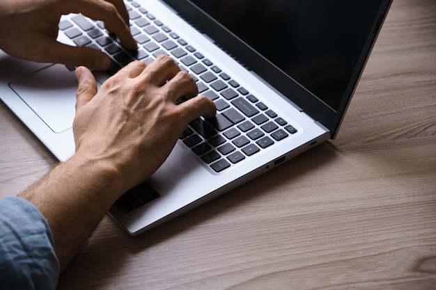 Mãos de homem digitando no teclado do laptop