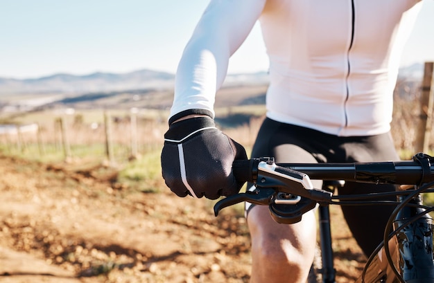 Mãos de homem e bicicleta na natureza rural e treinamento ao sol para esportes de triatlo e competição cardio Luvas de ciclista bicicleta e fitness ao ar livre para exercícios e corridas de maratona de ciclismo