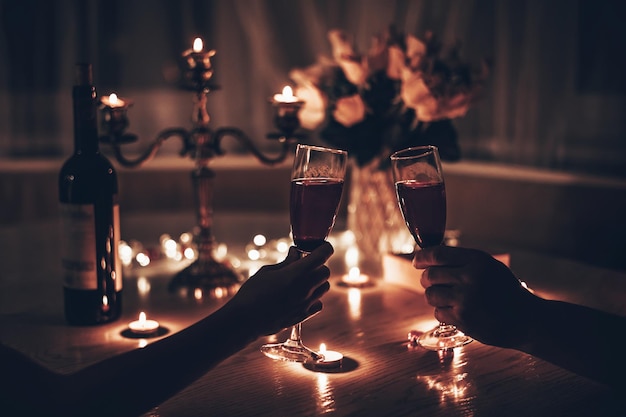 Mãos de homem e mulher segurando taças de vinho tendo um jantar romântico à luz de velas na mesa em casa Mãos de homem e mulher segurando uma taça de vinho Conceito de dia dos namorados ou encontro à luz de velas à noite