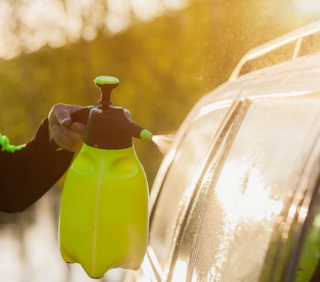 Foto mãos de homem lava seu carro com uma grande cabeça de água ao ar livre. limpeza e desinfecção. medidas de segurança durante a epidemia