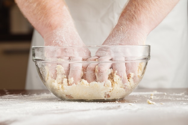 Mãos de homem preparando monte de massa de pão na mesa preta clara, revestida com farinha