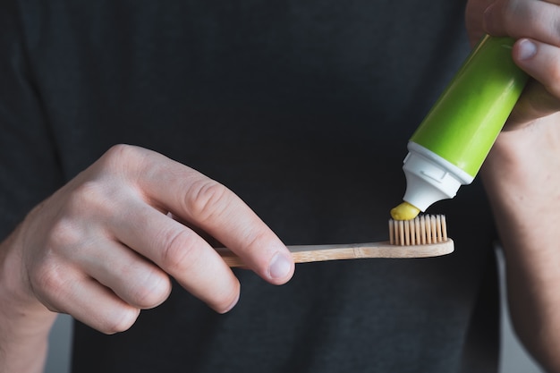 Foto mãos de homem segura escova de dentes de bambu com pasta de dentes verde. higiene dental