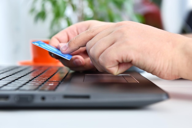 Foto mãos de homem segurando um cartão de crédito azul e comprando produtos online