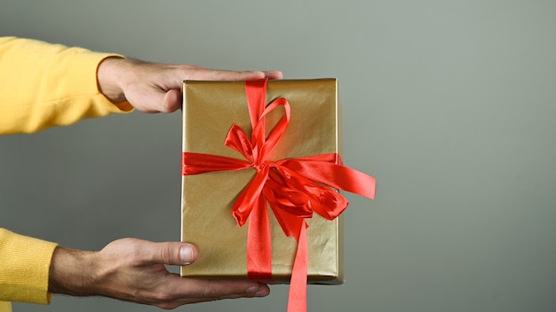 Mãos de homem segurando uma caixa de presente com um laço vermelho