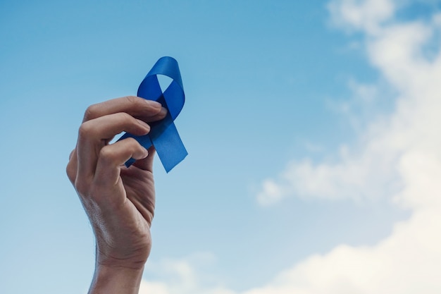Mãos de homem segurando uma fita azul sobre o céu azul, conscientização do câncer de próstata, novembro azul