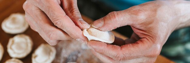 Mãos de homem sênior cozinhando e moldando pequenos bolinhos de massa crus caseiros com carne na mesa da cozinha. cozinha tradicional russa nacional. vista do topo.