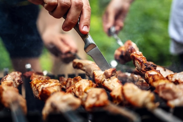 Mãos de homem tentando churrasco deliciosa carne grelhada com faca se preparando no piquenique da natureza com carne de porco