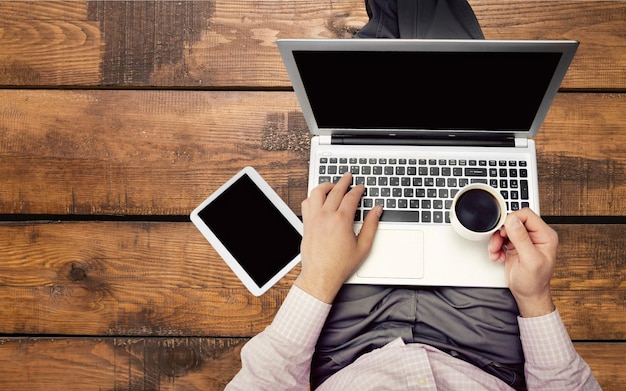 Mãos de homem usando laptop e segurando uma xícara de café