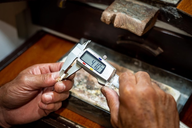 Foto mãos de joalheiro medindo e verificando o tamanho da jóia de ouro com a ferramenta de pinça vernier o ourives trabalhando criando em sua oficina de jóias