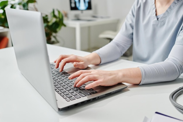 Mãos de jovem médica ou outro especialista digitando no teclado do laptop